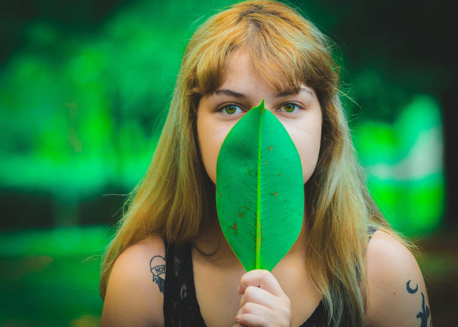 A young woman in a summer portrait holding a green leaf in a lush forest setting.